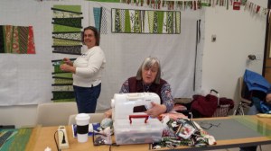 Jane Hann Morey, Liaison to Pine Tree Quilt Guild, and Membership Person to MMQG, left and Karen B., outgoing Co-Sec., working on wedge table runners